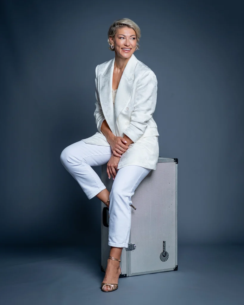 Retrato de Mariana Zhytariuk sentada sobre una maleta de fotografía con traje de chaqueta blanco en el estudio