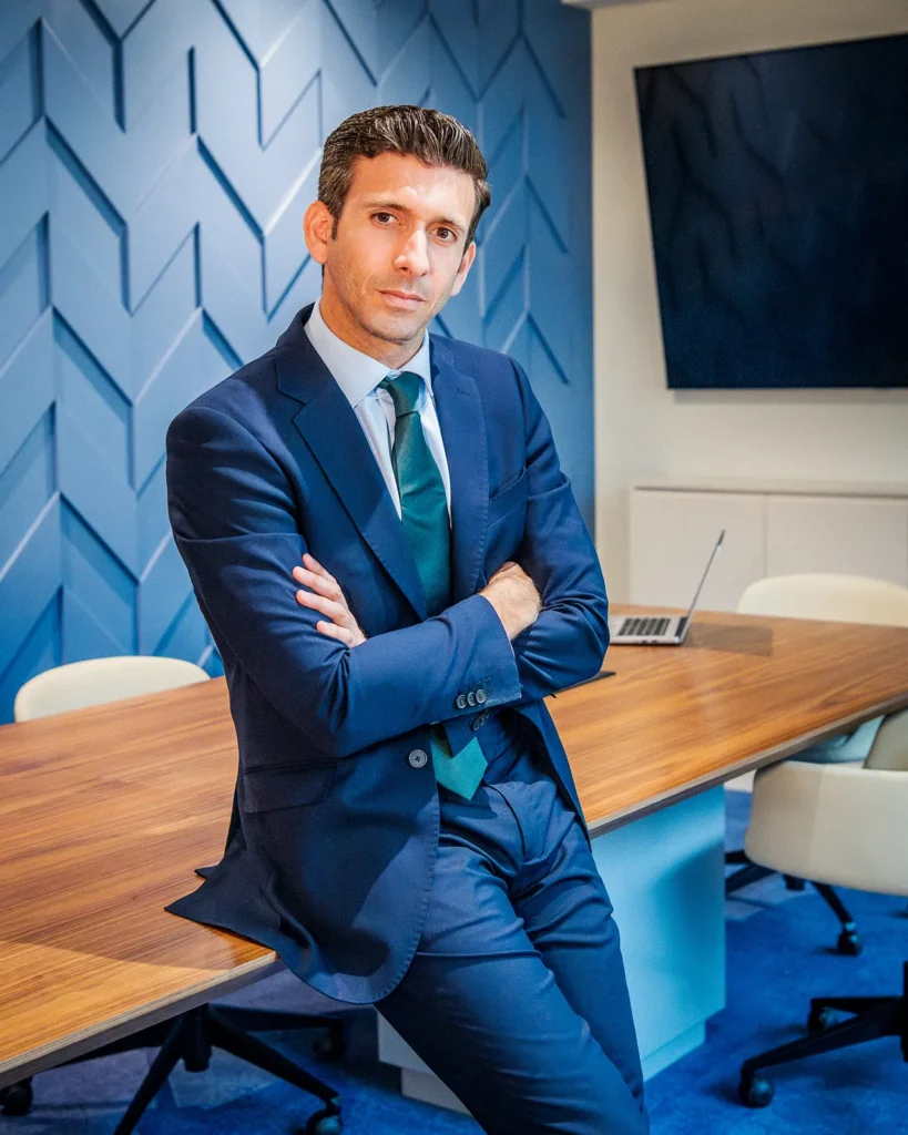 Retrato de Javier Nicolas con traje azul marino apoyado en una mesa de conferencias.