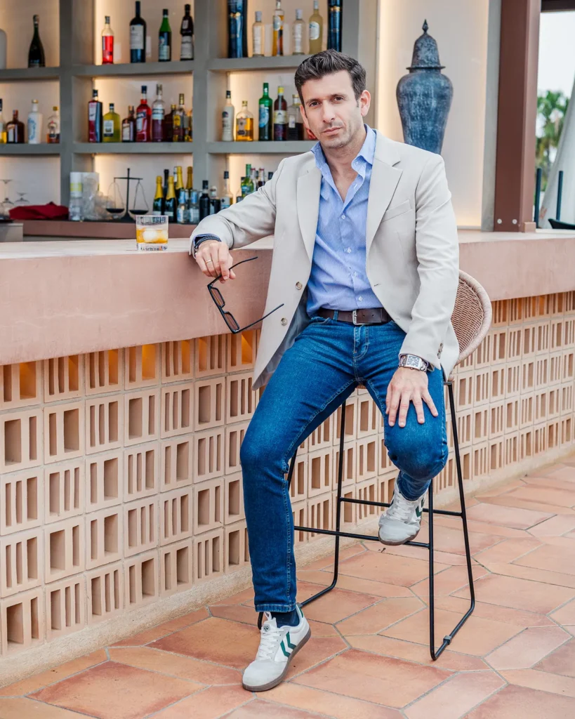 Retrato de Javier Nicolas con camisa y americana apoyado en la barra de un bar.