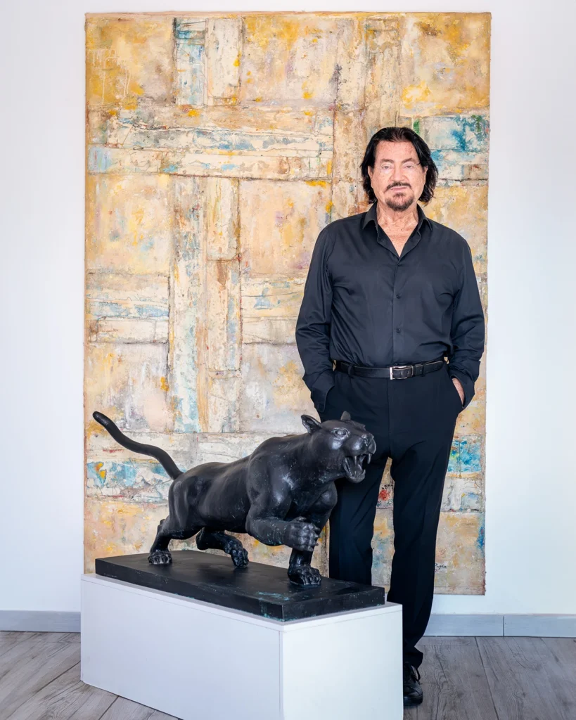 Retrato de Ginés Serrán Pagán junto a una de sus pinturas y una escultura de bronce de un puma.