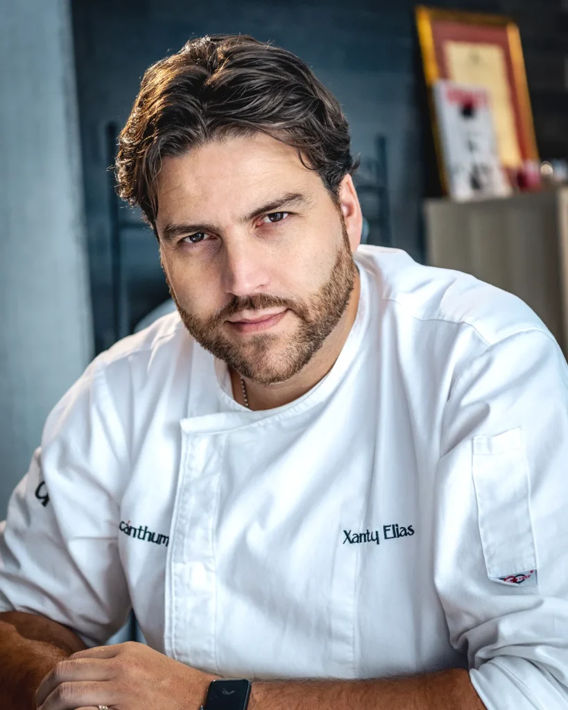 Retrato de Xanty Elías sentado en su oficina con su chaquetilla de chef.