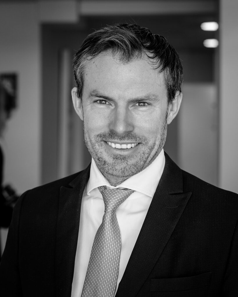 Retrato en blanco y negro de Kai Kaye con traje y corbata en su oficina.